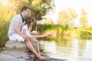 yound father and daughter sitting beside a lake