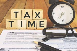 tax return with alarm clock and wooden blocks spelling: "tax time"