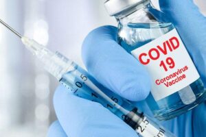 Gloved hand holding COVID-19 vaccine bottle and syringe