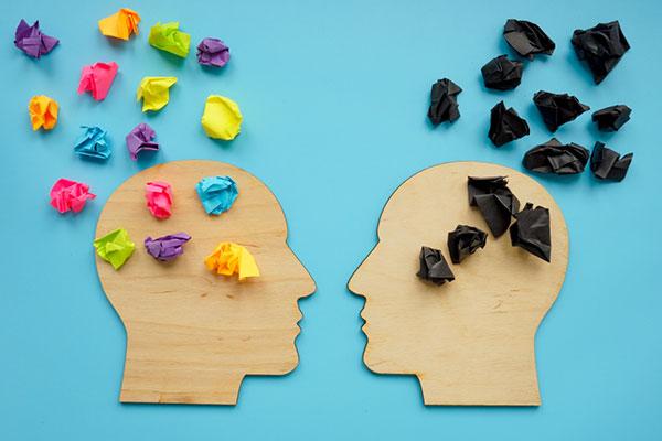 Avoid burn out by learning to think positively: one head with black pieces of paper (negative thoughts) and the other with colorful paper (positive thoughts)